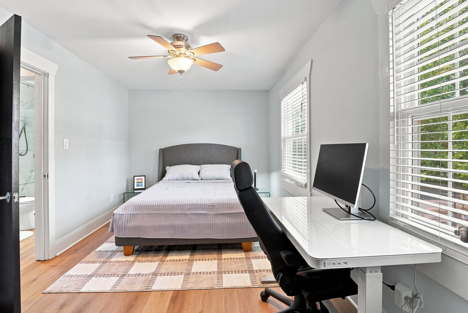 Queen bed beside a desk and windows